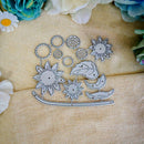 A set of silver metal die-cut craft embellishments, including sunflowers, leaves, and crescent moons, arranged on a textured beige fabric background with decorative flowers.