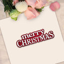 A square cream card with the words 'merry CHRISTMAS' in white lettering outlined in dark red, styled with pink roses and green leaves at the top on a light fabric background.