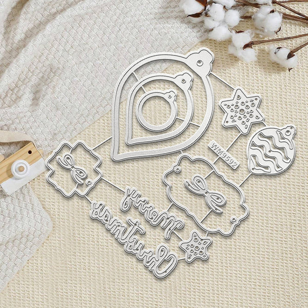 A flat-lay of a metal die-cutting or crafting template set featuring Christmas-themed shapes, including ornaments, stars, and cursive text, arranged on a textured cream fabric with cotton stems.