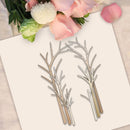 A flat-lay of a metal die-cut craft template featuring four leafy branch or vine shapes, placed on a cream cardstock with pink flowers in the background.