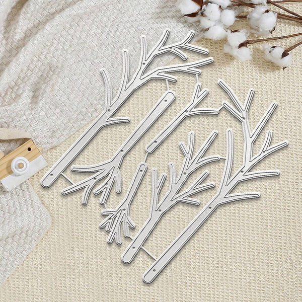 Four silver metal tree branch cutters arranged on a textured cream fabric background with cotton stems and a small wooden tag as styling props.
