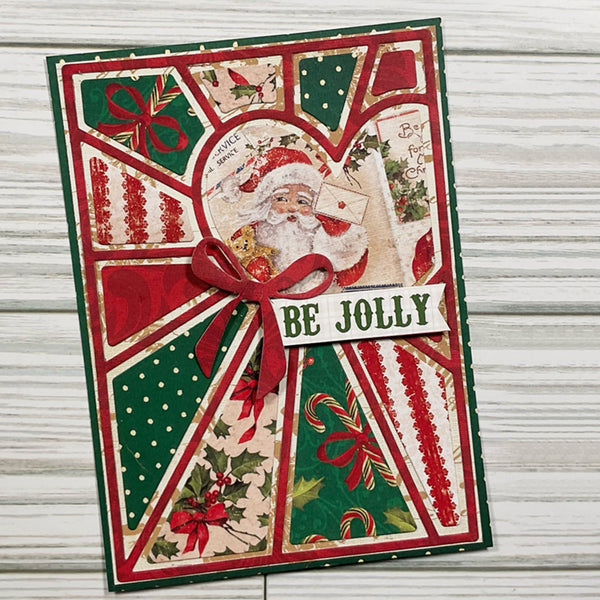 A handmade Christmas greeting card featuring a collage of festive patterns including red and green geometric panels, holly, candy canes, and a central Santa illustration with a red ribbon bow and a banner reading 'BE JOLLY'.