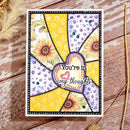 A handmade greeting card with a stained-glass style design featuring sunflowers, purple dotted patterns, yellow swirls, and a central heart-shaped cutout with the words 'You're in my thoughts'. The card is displayed flat on a rustic wooden surface with dried grass props.