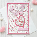 A handmade pink and white anniversary card with a butterfly and heart design, displayed on a white wooden surface with decorative pink and white accessories.