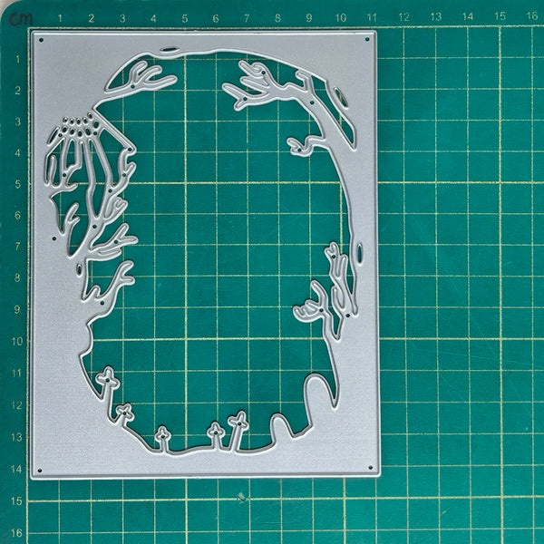 A silver metal die-cutting template with a coral reef and sea life silhouette design, displayed on a green cutting mat with measurement markings.