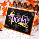 A handmade Halloween greeting card featuring the word 'spooktacular' in purple and yellow layered letters on a black background with white spiderwebs, styled with autumn leaves and a picket fence backdrop.