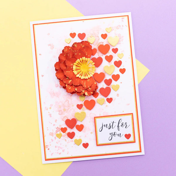 A handmade greeting card featuring a 3D layered red flower with a yellow center, scattered red and yellow hearts, and the text 'just for you' in a small white box, displayed on a yellow and purple background.