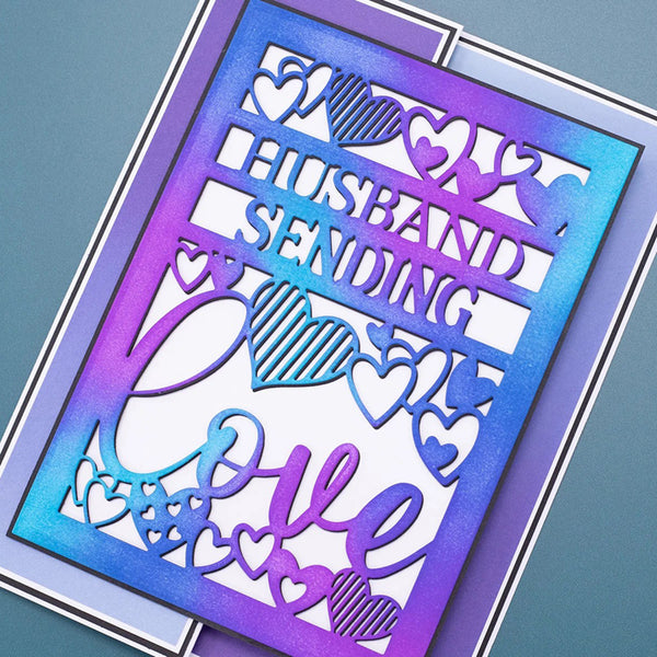 A layered card with a holographic blue-to-purple gradient border and cutout text reading 'HUSBAND SENDING' above the word 'Love' in script, decorated with heart motifs, shown on a blue-gray background.