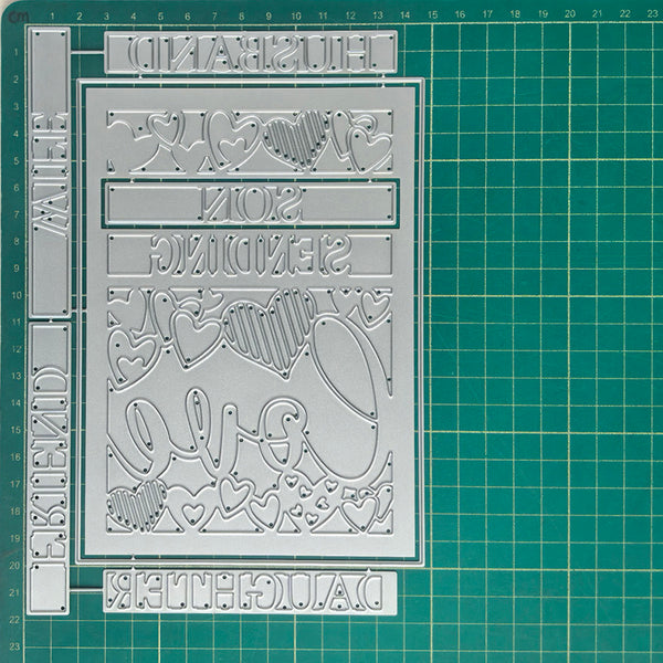 A silver metal stamping or embossing plate with decorative cutout lettering and hearts, shown on a green gridded cutting mat.