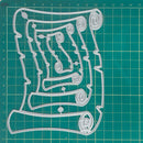 A clear plastic cookie cutter with an intricate scroll and loop design, displayed flat on a green cutting mat with grid lines.