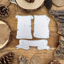 Three silver metal embossing or cutting dies shaped like vintage scroll and banner designs, arranged on a rustic wooden surface with pinecones and wood slices around them.