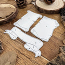 Four silver metal die-cut craft shapes with scroll and animal-like outlines, arranged on a rustic wooden surface with bark, pinecones, and dried leaves around them.