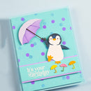 A handmade layered paper card featuring a penguin holding a purple umbrella, with small yellow and pink umbrellas and the text 'It's your Birthday' on a light blue background with purple polka dots.
