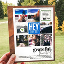 A handmade scrapbook card with a wooden frame and a collage of photos and text, held by a hand in an outdoor grassy setting.