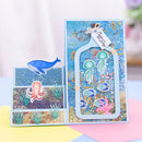 A handmade layered greeting card set with an ocean theme, featuring a large rectangular card with jellyfish and coral cutouts, a smaller square card with an octopus, and a separate blue whale sticker, displayed on pastel paper.