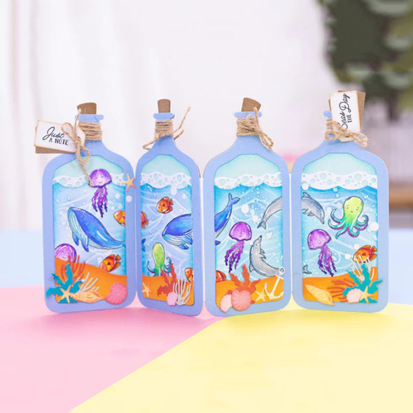 Four decorative glass bottles with cork stoppers, each filled with colorful underwater artwork showing dolphins, octopus, jellyfish, coral, and sea life. The bottles are arranged on a pastel pink and yellow surface with a soft blurred white background.