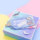 A decorative gift box with a layered pastel design in blue, purple, and teal, featuring a bottle-shaped clear window containing blue glitter and a card that reads 'You are my anchor,' plus small sea-creature embellishments.