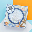 A square handmade greeting card with a nautical 'Sea you Soon' design, featuring a sailboat inside a porthole frame, seashells, an anchor, and glitter, photographed on a colorful blue, orange, and white background.