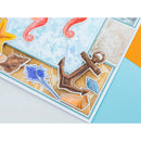 A close-up of a handmade greeting card featuring a nautical design with a brown anchor, blue starfish, orange seahorse, and seashell details layered over a light blue and beige background.