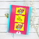 A handmade greeting card featuring a pink and white diagonal striped background with two yellow scalloped labels showing cherry ice cream sundae illustrations and the phrase 'You're the cherry on top!'. The card is displayed on a white wood background with decorative props.