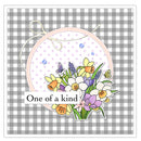 A square graphic design featuring a floral embroidery motif with spring flowers like daffodils, crocuses, and a purple lavender sprig inside a circular stitched frame. The design is layered over a gray and white gingham check background, with a white banner across the center reading 'One of a kind'.