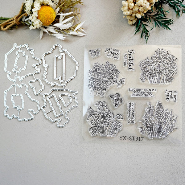 A clear acrylic stamp set with floral and butterfly illustrations and black printed phrases, shown next to six matching metal die-cut shapes on a light neutral background with dried flowers and greenery as props.