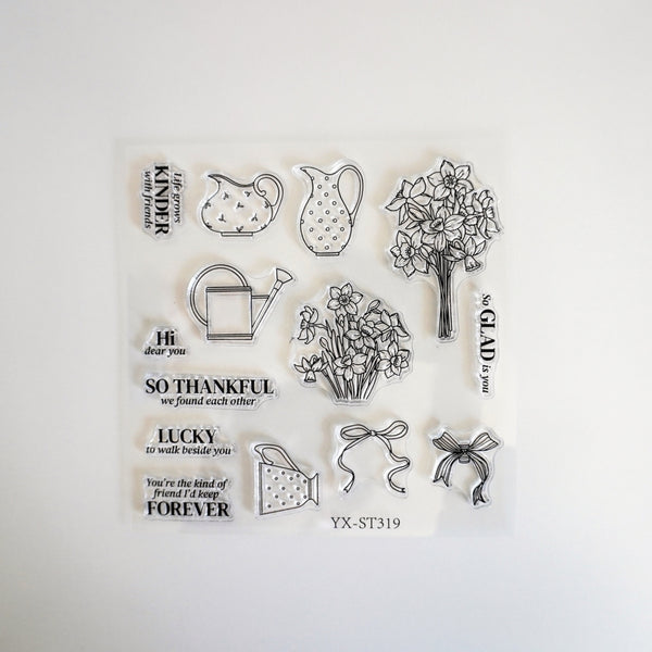 A clear plastic sheet of transparent stamps with black printed designs, including floral bouquets, watering cans, bows, and inspirational quotes, displayed on a white background.
