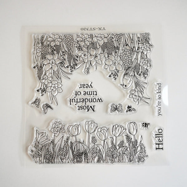A clear acrylic stamp set featuring black floral and botanical line art, tulip fields, butterflies, and phrases like 'Most wonderful time of year,' 'Hello,' and 'you're so kind,' shown on a plain white background.