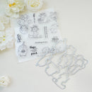 A clear stamp sheet with black cartoon bear illustrations and phrases, placed on a white surface with matching metal die-cut shapes beside it. White flowers decorate the corners of the scene.