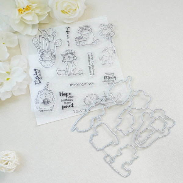 A clear stamp sheet with black cartoon bear illustrations and phrases, placed on a white surface with matching metal die-cut shapes beside it. White flowers decorate the corners of the scene.