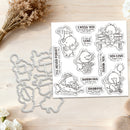 A clear stamp set and matching die cut outlines displayed on a light wood surface with dried flowers and white blossoms. The stamp sheet features cartoon animals and phrases such as 'I MISS YOU', 'BIG LOVE', 'THANK YOU', and 'WARM HUG'.