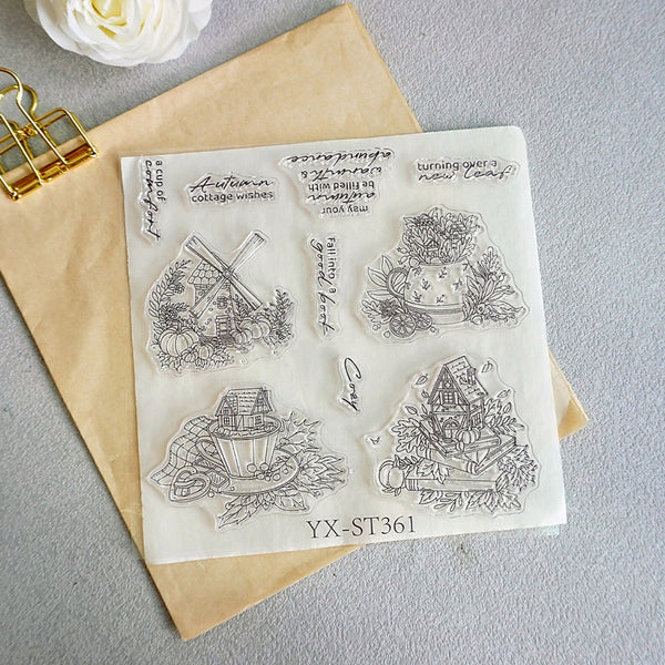 A clear stamp sheet with black line-art autumn-themed illustrations and text, placed on top of a kraft paper envelope. The sheet includes designs such as a windmill, pumpkins, a teacup, a small house, and decorative phrases.