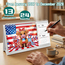 A desktop calendar displayed on a wooden table, showing a patriotic 2024/2025 page with an American flag background and a cartoon cow in red, white, and blue. A hand is turning the page with a black pen, with a coffee cup, books, and glasses nearby.