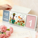 Desk calendar with floral design and hand holding it, surrounded by pink flowers and a card.