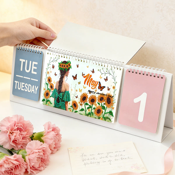 Desk calendar with floral design and hand holding it, surrounded by pink flowers and a card.