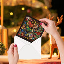 A person's hands hold a Christmas-themed beaded card with a black background and colorful embellishments, partially pulled from a white envelope. The background shows a softly blurred festive holiday scene with warm lights and a deer figurine.
