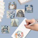 A hand holds a white pen over a lined notepad printed with 'Best Wishes' and a floral wreath, surrounded by six small square winter-themed art prints featuring Santa, a polar bear, ornaments, a Christmas tree, a snowman, and a snowy building. The scene is styled on a light blue background with partial props visible at the edges.