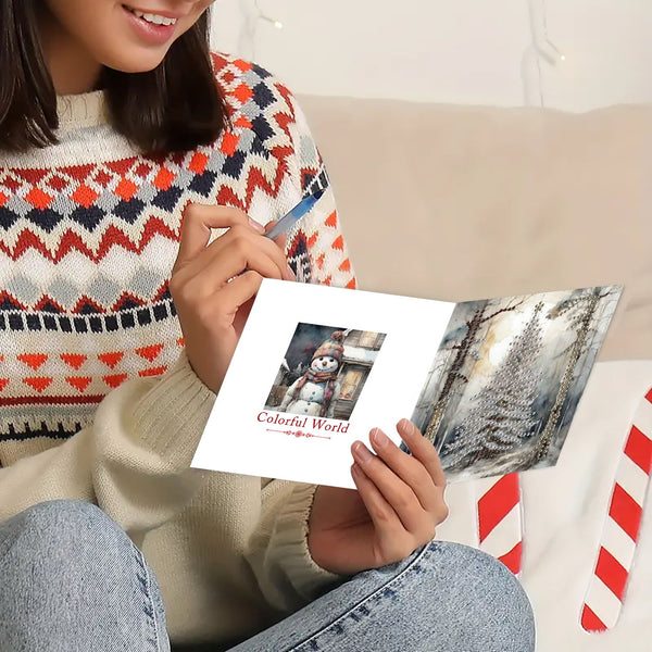A person holding an open greeting card with a winter scene and the text 'Colorful World' in a cozy indoor setting. The person is wearing a patterned knit sweater and blue jeans.