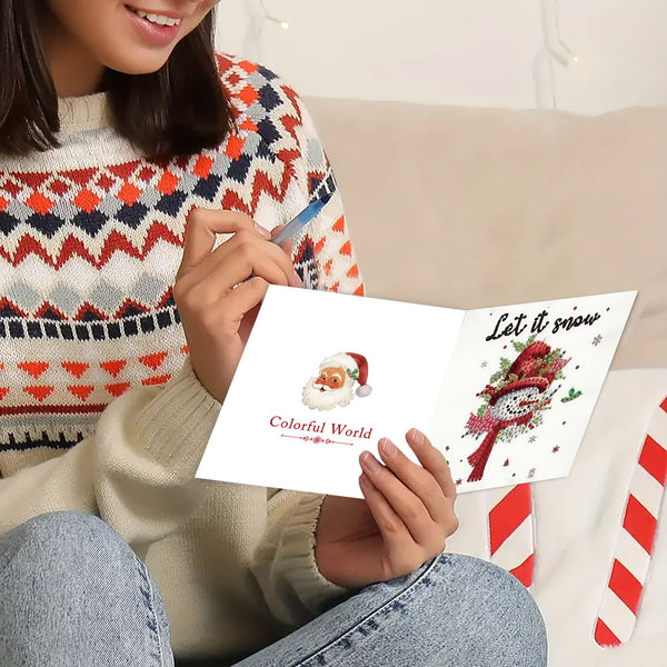 A person sitting indoors holds an open greeting card. The card shows a Santa illustration on one side and a snowman with the text 'Let it snow' on the other.