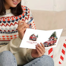 A person in a patterned knit sweater holds a white greeting card featuring two red vintage trucks carrying Christmas trees, with the text 'Colorful World' on the card.