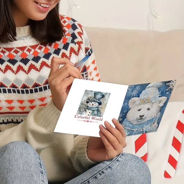 A person holding a white greeting card with a winter illustration, seated on a couch. The person wears a multicolor knit sweater and blue jeans, with a red-and-white striped candy cane visible nearby.