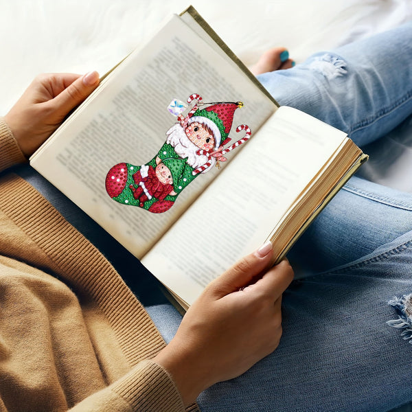 A person holding an open book with printed text, featuring a Christmas-themed pop-up page insert shaped like a green stocking with Santa and a child, styled on blue jeans and a beige sweater.