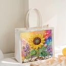 A clear plastic tote bag with white handles, featuring a colorful diamond painting design of a sunflower and purple flowers on a bright rainbow background.