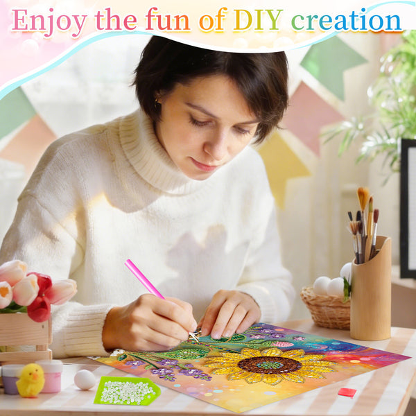 A woman in a cream knit sweater is shown from the chest up, focused on painting a colorful sunflower design on a sheet of paper. She is holding a pink-handled craft tool.
