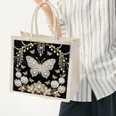 Tote bag with decorative butterfly and floral design held by a person wearing a striped shirt.
