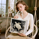 Woman holding a tote bag with a turtle design in a home setting