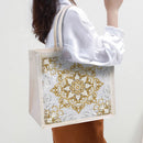 Tote bag with gold and white floral pattern held by a person wearing a white shirt.