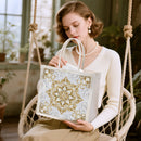 Woman holding a decorative bag with intricate gold patterns in a cozy indoor setting.