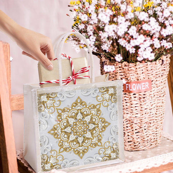 Decorative gift bag with gold mandala design held by a hand, next to a basket of flowers.