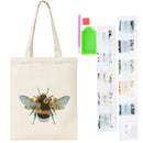 Beige canvas tote bag with a beehive and yellow flowers embroidered design, shown with a diamond painting kit including beads, a green palette, and two pink sticks on a white background.